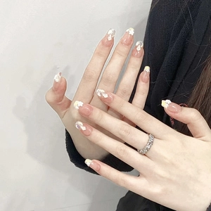 Nahaufnahme von nude-rosa Klebenägeln mit weißen 3D-Blumen und Glitzer-Details