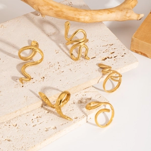 Detail of gold snake rings with scale textures on a natural stone and wood background