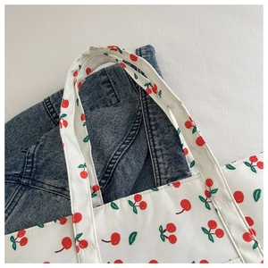 Close-up of white tote bag with red cherry pattern on dark denim background fabric