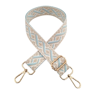Detail of adjustable woven jacquard bag strap with beige and blue patterns and gold hardware