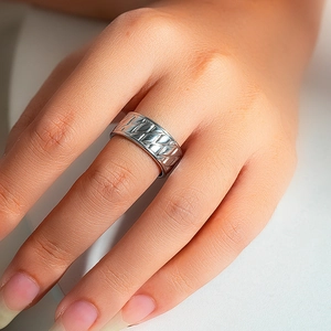 Detail of a wide silver-tone ring with diamond-shaped cross engravings on index finger