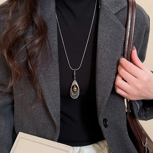 Long silver chain necklace with a tiger eye stone pendant on a model in a grey suit