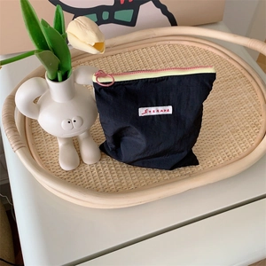Close-up of black nylon makeup bag with contrast zippers on a vintage rattan tray