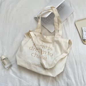 Detail of off-white canvas tote bag with brown embroidered text and adjustable strap