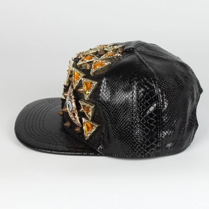 Λεπτομέρεια μαύρου snapback από δέρμα φιδιού με χρυσά καρφιά και κεχριμπαρένιες πέτρες