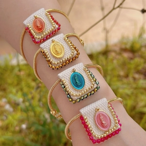 Religious woven bracelet set with gold chains and colorful saint charms worn on a wrist