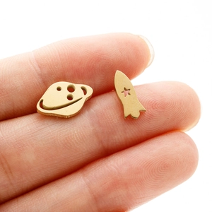 Detailed close-up of asymmetrical golden stainless steel rocket and planet stud earrings