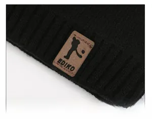 Close-up of black chunky knit texture with a brown leather logo patch on a winter hat