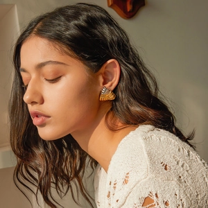 Detail of model wearing gold and silver woven texture fan-shaped earrings with sunlight