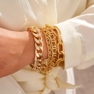 Close-up of stacked gold chain bracelets with textured links and glossy metallic finish