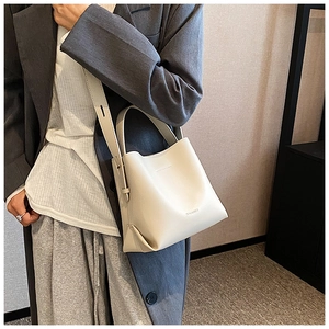 Detail view of cream white leather bucket bag with top handle and logo on casual model
