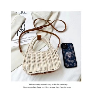 White semi-circular woven straw crossbody bag with brown leather handles and gold hardware