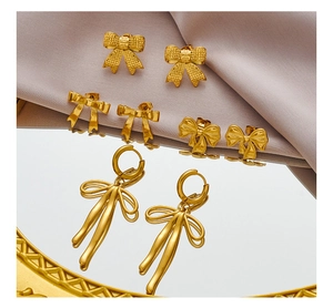 Detailed view of four pairs of golden bow earrings on silk fabric with mirror reflection