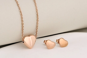 Close-up of polished rose gold heart pendant necklace and matching stud earrings set
