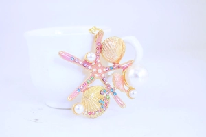 Detail of starfish and shell keychain with pink rhinestones and white pearls on gold metal
