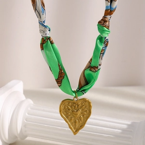 Detail of 18K gold heart pendant with sunburst design on a green silk ribbon necklace