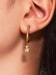 Detail showing a gold-plated hoop earring with a sparkling girl-shaped zircon pendant