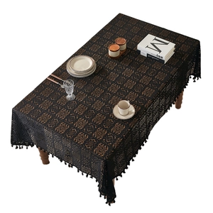 Elegant black lace crochet tablecloth with decorative tassels on a wooden dining table