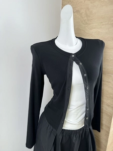 Detail of a black ribbed knit cardigan with buttons, shown on a mannequin in a layered style