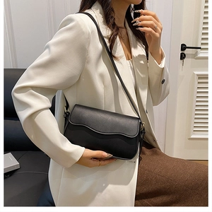 Detail of minimalist black square shoulder bag with wavy flap design on white blazer