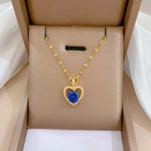 Detail of gold heart pendant with blue center stone and white gems in a brown jewelry box