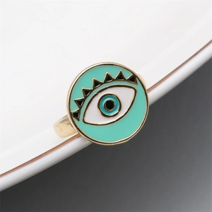 Macro shot of gold evil eye ring with mint green and blue enamel details on ceramic