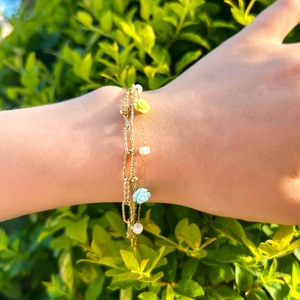 Bohemian gold layered bracelet featuring floral accents and white beads on model wrist