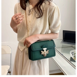 Detail of green snakeskin crossbody bag featuring gold bee clasp and chain strap
