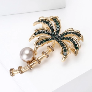 Detailed view of a gold palm tree brooch with green crystals and a pearl accent
