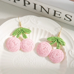 Detail shot of handmade woven pink cherry earrings on a white embossed porcelain plate