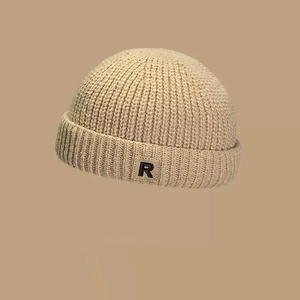 Detalle de gorro de punto beige con borde doblado y etiqueta negra con la letra R