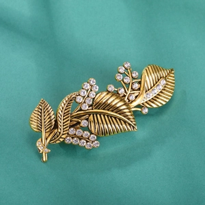 Vintage gold leaf hair clip featuring sparkling white rhinestones on a green background