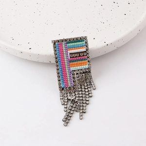 Macro shot of colorful rhinestone F-letter brooch with long shimmering fringes on a ceramic plate