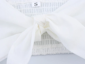 Detail eines weißen Crop-Tops mit Knotendesign vorne und plissierter elastischer Stoffstruktur
