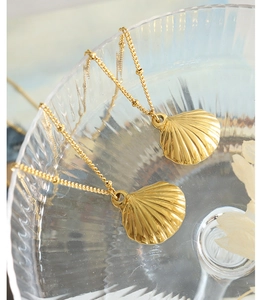 Detailed close-up of two gold scallop pendant necklaces with delicate bead chains
