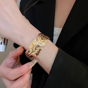 Detail view of a gold leaf-shaped open cuff bracelet featuring a polished metallic finish
