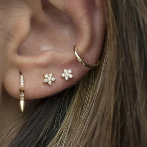 Close-up of golden flower stud earrings and helix cuff with zircon on ear