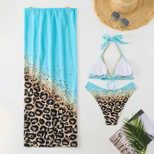 Flat lay of a three-piece leopard print bikini set with metal chain straps and sarong