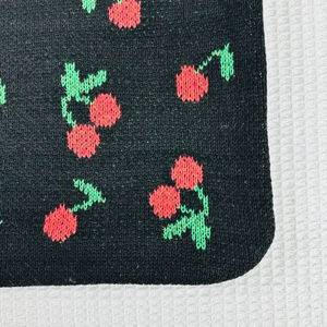 Macro shot of black knit fabric featuring red cherry patterns and green leaf texture