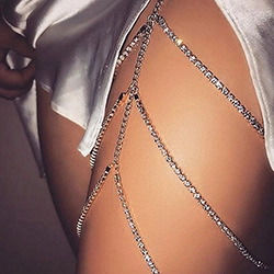 Macro shot of silver multi-layer rhinestone thigh chain jewelry on skin with white satin