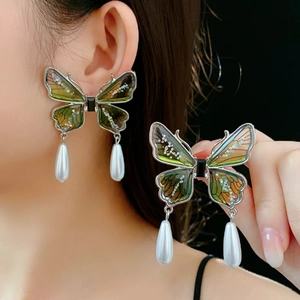Detailed view of butterfly earrings with green gradient wings and hanging white pearl