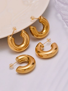 Detailed close-up of thick gold-plated hollow C-shaped hoop earrings on ceramic tray