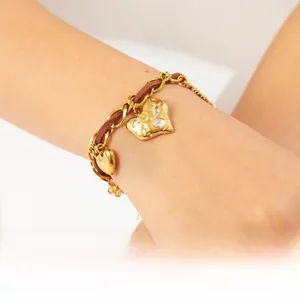 Close-up of gold chain and brown cord bracelet with crystal heart pendants on wrist