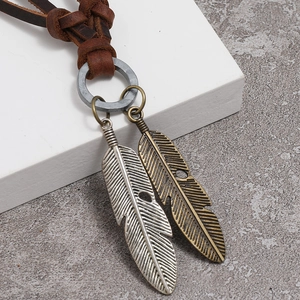 Macro detail of retro leather cord and dual-tone feather pendants on a textured surface