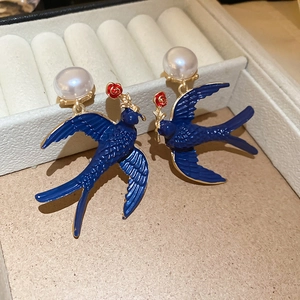 Detail view of swallow and water drop pearl earrings with blue enamel and red floral accents