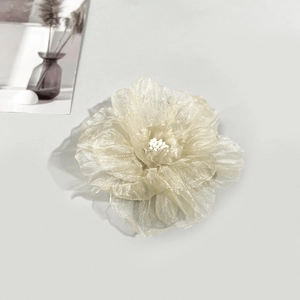 Gros plan d'une pince à cheveux camélia en organza beige aux pétales superposés