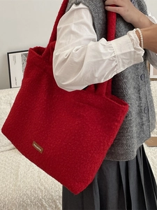 Red plush tote bag in soft lamb wool texture worn by a model in a cozy home setting