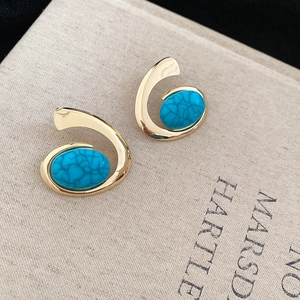 Close-up of golden irregular earrings with oval turquoise resin stones on a book