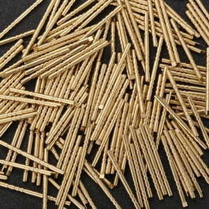 Precision brass connector pins with circular knurling patterns in a bulk pile