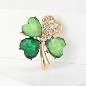 Macro shot of gold clover brooch with green cracked stone and clear crystal rhinestones